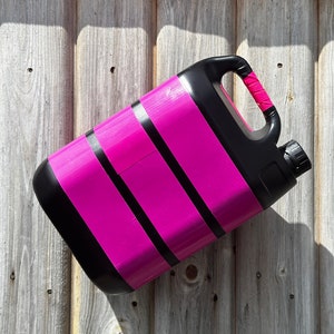 Può includere: Un contenitore di plastica nero con un design a strisce rosa e nere. Il contenitore ha una maniglia e un beccuccio.
