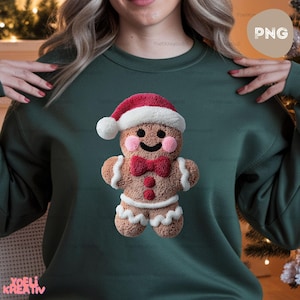 May include: Dark green sweatshirt featuring a gingerbread man design. The gingerbread man is wearing a Santa hat and a red bow tie. The design is detailed with white icing and pink cheeks, perfect for the holiday season.