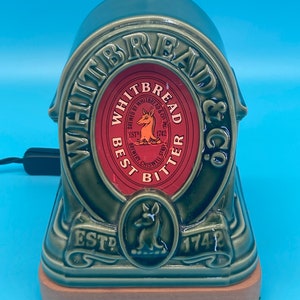 May include: A green ceramic lamp shaped like a loaf of bread with the Whitbread & Co. logo and the text "Best Bitter" in red. The lamp has a wooden base and a cord.