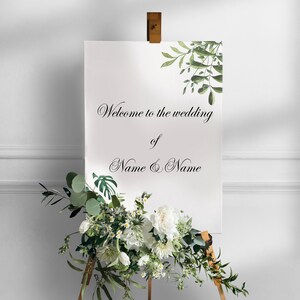 May include: White wedding sign with green foliage and the text "Welcome to the wedding of Name & Name"