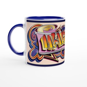 May include: A white ceramic mug with a blue handle and rim. The mug features a colourful graffiti-style design with the word "WAKE" in yellow, orange, and pink, set against a cream background with blue, purple, and gold accents.