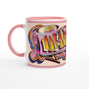 May include: A white ceramic mug with a pink handle and interior. The mug features a colourful graffiti-style design with the word "WAKE" in yellow and orange, outlined in black, on a pink background with a retro design.