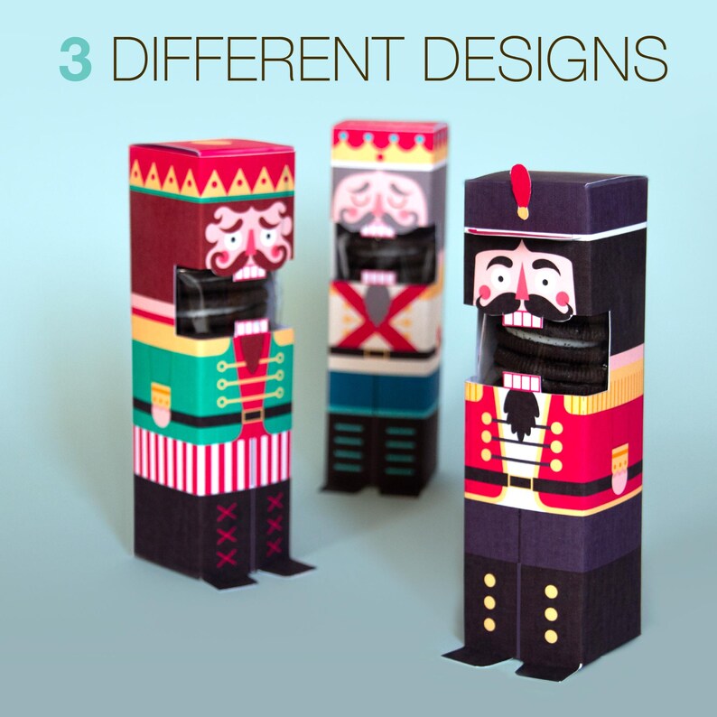 May include: Three decorative nutcracker-themed boxes in different designs. The boxes are rectangular and feature colorful illustrations of nutcracker soldiers. The text "3 DIFFERENT DESIGNS" is at the top. The boxes are on a light blue background.