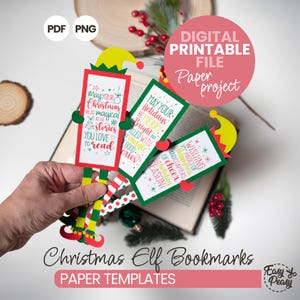 May include: Christmas Elf Bookmarks paper templates. The image displays a hand holding several colourful elf-themed bookmarks. Each bookmark has a rectangular design with festive text like "May your Christmas be magical" and "Wishing you pages of cheer". The bookmarks are set against an open book.