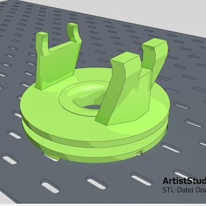 Könnte beinhalten: Ein grünes 3D-gedrucktes Objekt mit zwei U-förmigen Armen. Das Objekt befindet sich auf einer grauen Oberfläche mit einem Gittermuster.