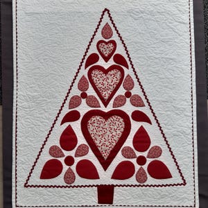 May include: A red and white quilted Christmas tree wall hanging with a scalloped edge. The tree is made up of hearts and teardrop shapes.
