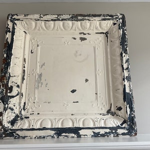May include: A white ceiling tile with a decorative, embossed design. The tile is distressed and has a black border.