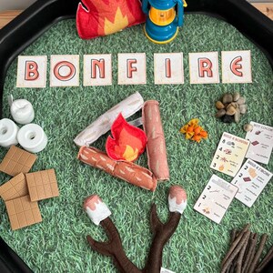 Puede incluir: Un juego infantil con tem&aacute;tica de hoguera. Incluye llamas de fieltro, una linterna azul y la palabra "BONFIRE" deletreada con fichas de letras. Tambi&eacute;n presenta troncos de fieltro, malvaviscos, galletas Graham y tarjetas.