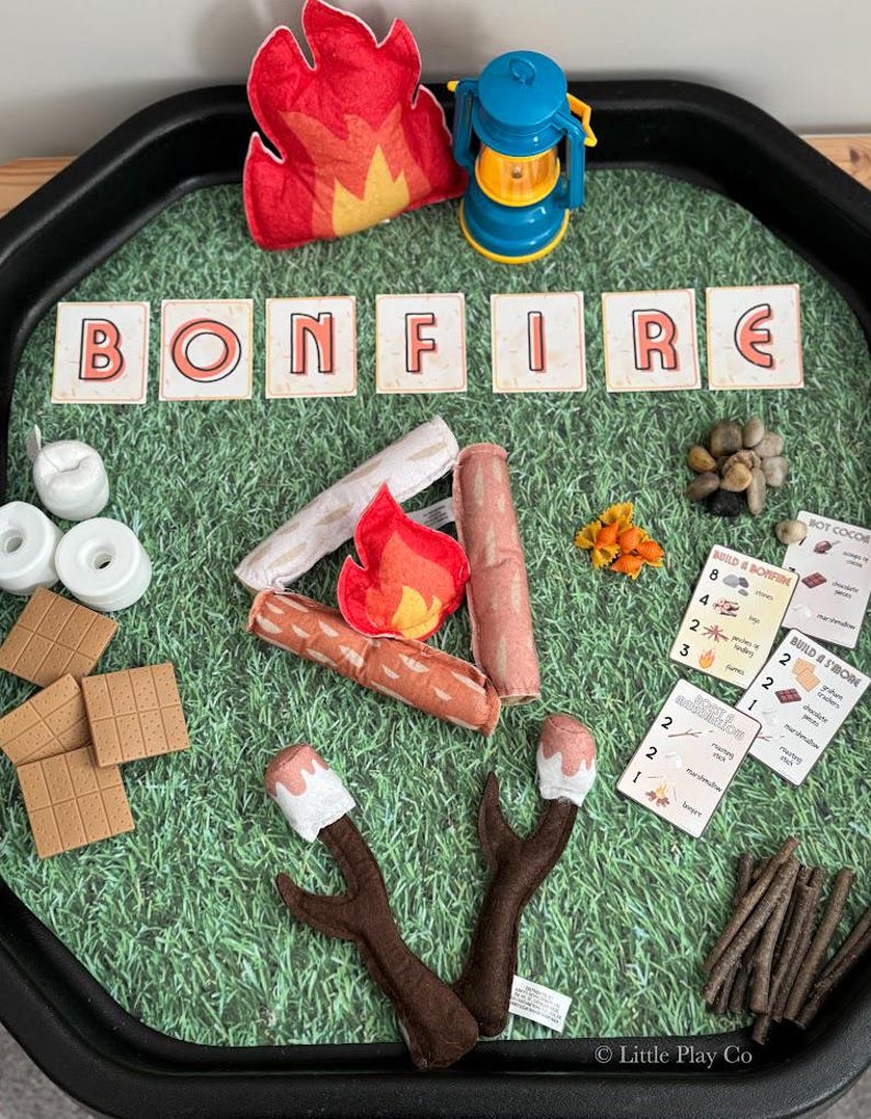 Puede incluir: Un juego infantil con tem&aacute;tica de hoguera. Incluye llamas de fieltro, una linterna azul y la palabra "BONFIRE" deletreada con fichas de letras. Tambi&eacute;n presenta troncos de fieltro, malvaviscos, galletas Graham y tarjetas.