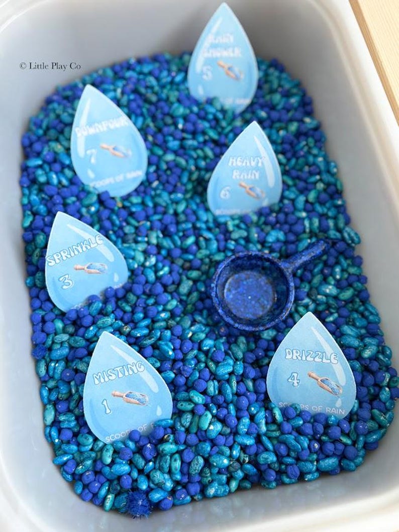 May include: A sensory bin filled with blue and teal beans, featuring raindrop-shaped cards labeled with rain intensity terms like "Misting" and "Heavy Rain." A small blue scoop is also included, perfect for educational play.