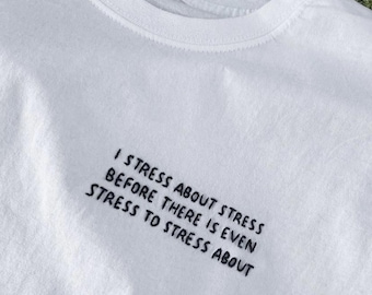 Puede incluir: Camiseta blanca con texto bordado en negro que dice "Me estreso por el estrés antes de que incluso haya estrés por el que estresarme."