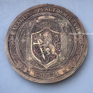 Pode incluir: Uma placa de parede circular em tons de bronze com um relevo intrincado de um leão segurando uma espada e em pé sobre uma serpente. O texto "MAKE NO PEACE WITH EVIL" está inscrito no topo e "GAL 5:24" impresso na parte inferior.