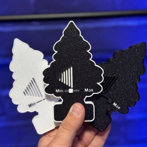 以下が含まれることがあります： 白と黒のツリー型芳香剤3つ。質感のあるキラキラした仕上げで、それぞれにMinとMaxの文字が入った水平スライダーのグラフィックがあり、調整可能なレベルを示しています。デザインは重なっており、白いものが1つと黒いものが2つあります。