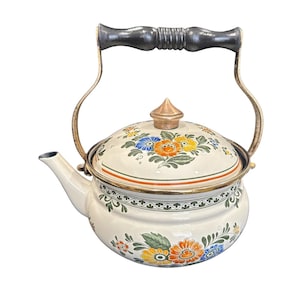 May include: Cream-colored enamel teapot with a floral design in orange, blue, and yellow. The teapot has a black wooden handle and brass accents. The lid is topped with a copper-colored finial. A decorative kitchenware item.