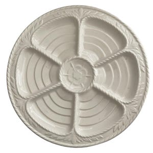 May include: A round, off-white ceramic serving platter featuring six distinct, wedge-shaped compartments radiating from a central circular section. The rim and dividers are decorated with a raised rope-like texture and leaf motifs.
