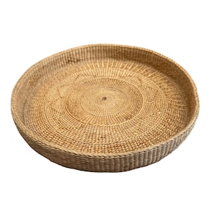 May include: A round, shallow tray crafted from woven light brown natural fibers. The tray features a tight, concentric circular weave pattern across the flat base and a sturdy, upright rim that creates a defined edge for the circular structure.