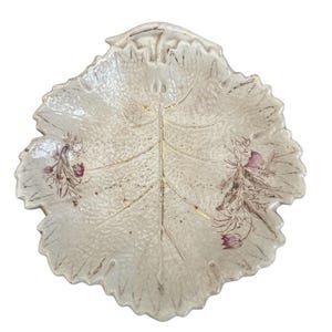 May include: Cream-colored, leaf-shaped decorative dish with a textured surface. The dish features gold accents along the central vein and edges, with delicate floral and foliage designs in shades of pink and brown.
