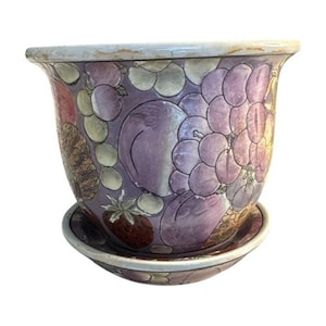 May include: A ceramic flower pot with a matching saucer. The pot is decorated with a colorful fruit design, featuring grapes, plums, and strawberries in shades of purple, red, and green. The rim and saucer edge have a light beige trim.