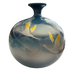 May include: A decorative, spherical vase with a dark teal neck and a rounded body. The vase has a gradient of colors, transitioning from teal to silver, with yellow accents. The vase is likely made of glass or ceramic.
