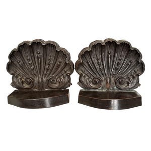 May include: Pair of dark brown, seashell-shaped bookends. Each bookend features a detailed, fan-like design with intricate lines and curves. The base is a simple, rectangular shape, providing stability. The bookends are made of a dark, possibly metal material.