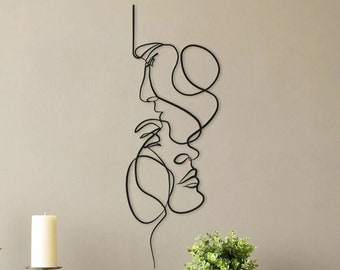 Puede incluir: Arte de pared de metal negro con un dibujo de línea de dos caras, una encima de la otra, con sus perfiles enfrentados. Las caras están conectadas por una línea continua.