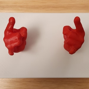 May include: Two red 3D printed hands with index fingers pointing upwards, mounted on a white surface.