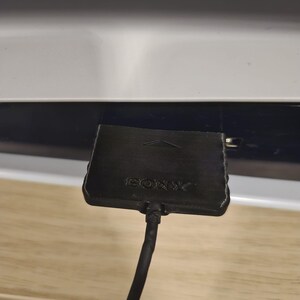May include: A black Sony adapter with a cable attached to it.
