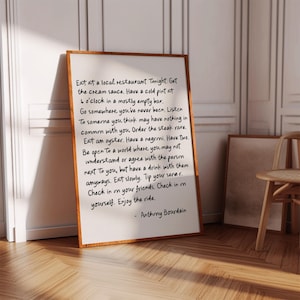 Puede incluir: Un cuadro rectangular con marco de madera marrón que contiene texto escrito a mano en negro sobre fondo blanco. El texto dice: Eat at a local restaurant Tonight. Get the cream sauce. Have a cold pint at 6 o'clock in a mostly empty bar. Go somewhere you've never been. Listen to someone you think may have nothing in common with you. Order the steak rare. Eat an oyster. Have a negroni. Have two. Be open to a world where you may not understand or agree with the person next to you, but have a drink with them anyways. Eat slowly. Tip your server. Check in on your friends. Check in on yourself. Enjoy the ride. - Anthony Bourdain