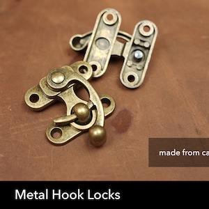 May include: Two antique gold metal hook locks, made from cast metal. The hook lock has a small knob and a hook that can be used to secure a bag, box, or other item.