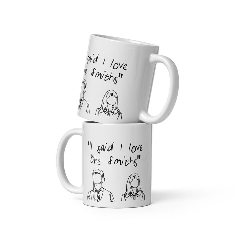 May include: Two white ceramic mugs stacked on top of each other. The top mug has the text "gaid I love he Smiths" written on it. The bottom mug has the text "I said I love The Smiths" written on it.