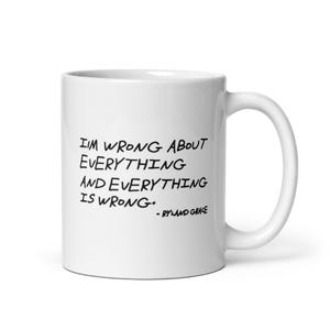 May include: A white ceramic mug featuring black handwritten-style text that reads: I'M WRONG ABOUT EVERYTHING AND EVERYTHING IS WRONG. - RYLAND GRACE. The mug has a standard cylindrical shape with a curved handle on the right side and a smooth finish.