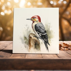 May include: Watercolor painting of a red-headed woodpecker perched on a tree branch. The bird has black and white stripes and a red crown. The background is a soft watercolor wash of green and blue.