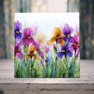 May include: A square decorative tile featuring a watercolor painting of irises. The flowers are in shades of purple, pink, and yellow, with green leaves and stems. The background is a soft, light blue.
