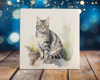 May include: Watercolor painting of a gray tabby cat sitting on a rock. The cat has green eyes and a white chest. The background is a soft watercolor wash of blue and green.