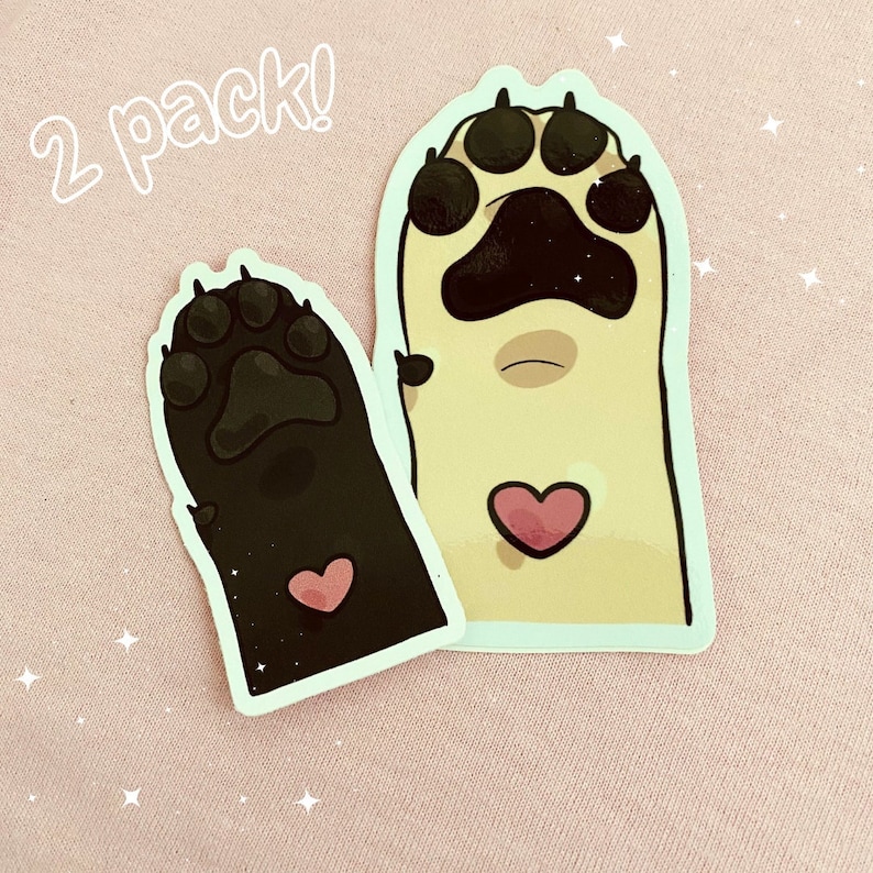 May include: Two paw print stickers, one black and one beige, with a pink heart on each. The stickers say "2 pack!" in white text.