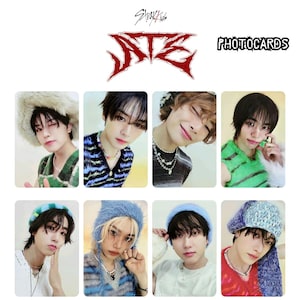 May include: A set of 8 photo cards featuring members of the K-pop group Stray Kids. The cards are printed with images of the members in various poses and outfits. The cards are all rectangular and have a white background. The text "Stray Kids" and "ATE" is printed in red at the top of the image. The text "PHOTOCARDS" is printed in white at the top right of the image.