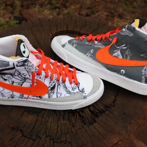 May include: A pair of white high-top trainers with orange accents. The trainers feature a black and white print of characters from the film "The Nightmare Before Christmas".