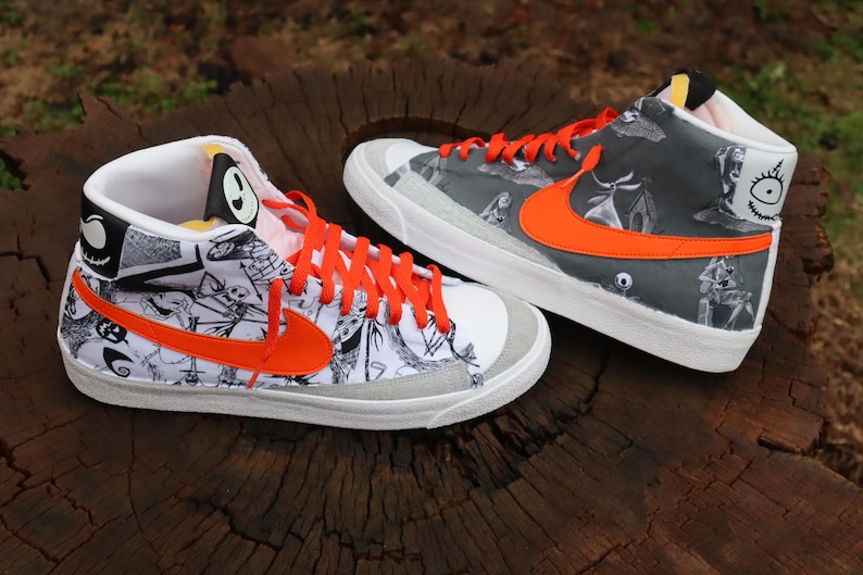 May include: A pair of white high-top trainers with orange accents. The trainers feature a black and white print of characters from the film "The Nightmare Before Christmas".