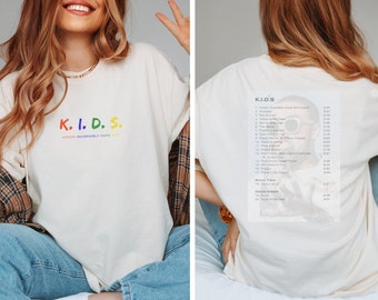 May include: White t-shirt with the text "K.I.D.S. KICKIN INCREDIBLY DOPE" printed on the front. The back of the shirt features a black and white photo of a person with the text "K.I.D.S." and a list of song titles.