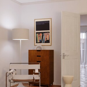 a modern living room with a minimalist design, featuring a white chair, a wooden dresser, and a framed poster on the wall.