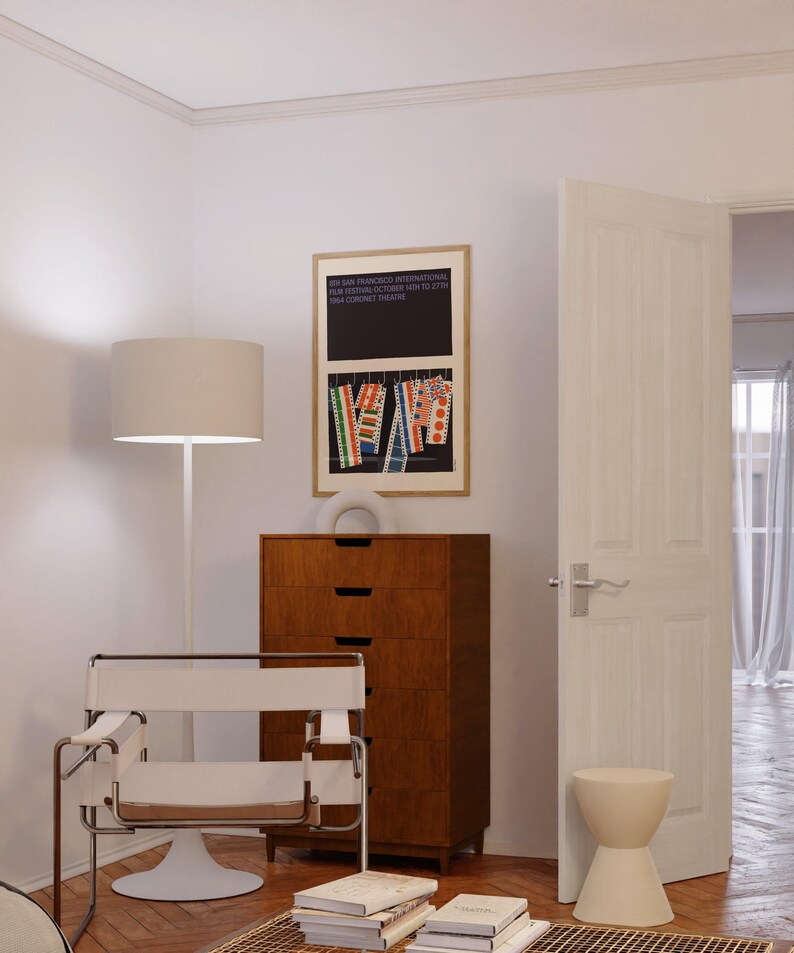 a modern living room with a minimalist design, featuring a white chair, a wooden dresser, and a framed poster on the wall.