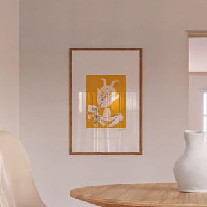 a wooden table with a white vase on it, and a framed artwork hanging on the wall above the table.