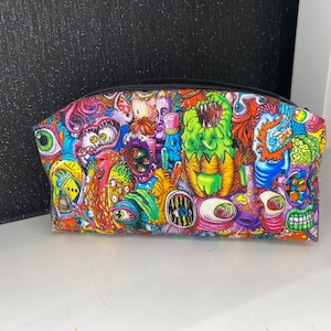 May include: A colorful zippered pouch with a psychedelic print of various cartoon creatures and eyes. The pouch is made of fabric and has a black zipper.