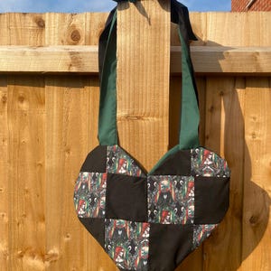 Peut inclure: Un sac en patchwork en forme de cœur avec un motif à carreaux noirs et verts. Le sac a une bandoulière verte avec un nœud noir en haut.