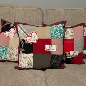 Pode incluir: Uma cole&ccedil;&atilde;o de almofadas de patchwork com uma variedade de padr&otilde;es e cores de tecido, incluindo florais, vermelho liso e tecidos estampados. Cada almofada tem uma borda vermelha escura e patches em forma de cora&ccedil;&atilde;o com texto bordado. Algumas almofadas t&ecirc;m patches retangulares adicionais com texto.