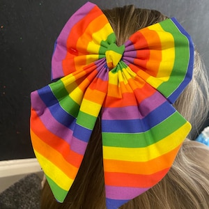 Könnte beinhalten: Eine regenbogenfarbene Stoffschleife mit einer Knotenmitte. Die Schleife ist aus weichem, farbenfrohem Stoff gefertigt und perfekt, um jedem Outfit einen Farbtupfer zu verleihen.