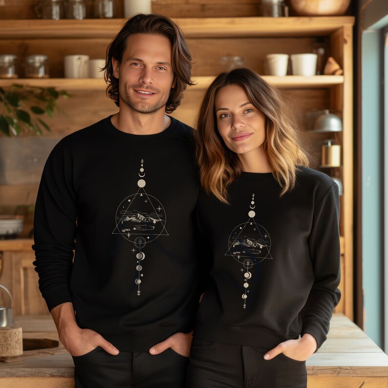 May include: Two people wearing black sweatshirts with a white graphic design of a mountain range, stars, and a crescent moon. The design is surrounded by a geometric pattern.