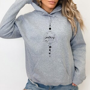 May include: A grey hooded sweatshirt with a black graphic design featuring a mountain range, a circle, a triangle, and a series of moons and stars.