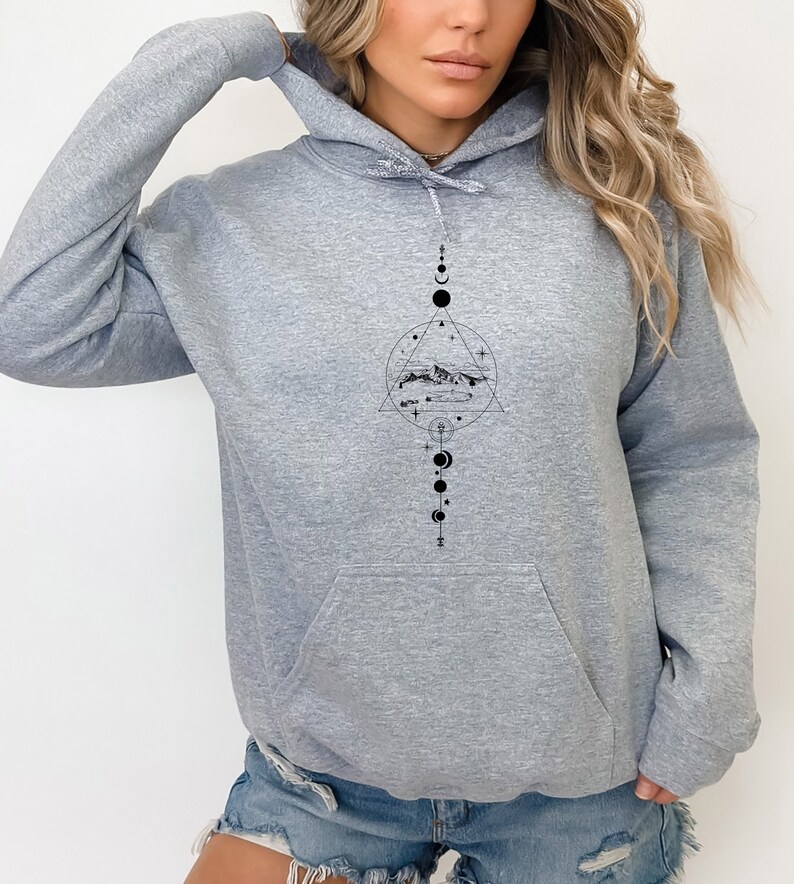 May include: A grey hooded sweatshirt with a black graphic design featuring a mountain range, a circle, a triangle, and a series of moons and stars.