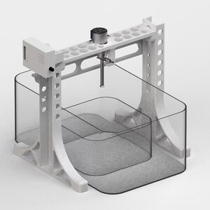 May include: A white, industrial-style apparatus with a clear, curved container. The structure has a top section with multiple holes, a central rod, and a lower container with a gray interior. The design suggests a scientific or laboratory setting.